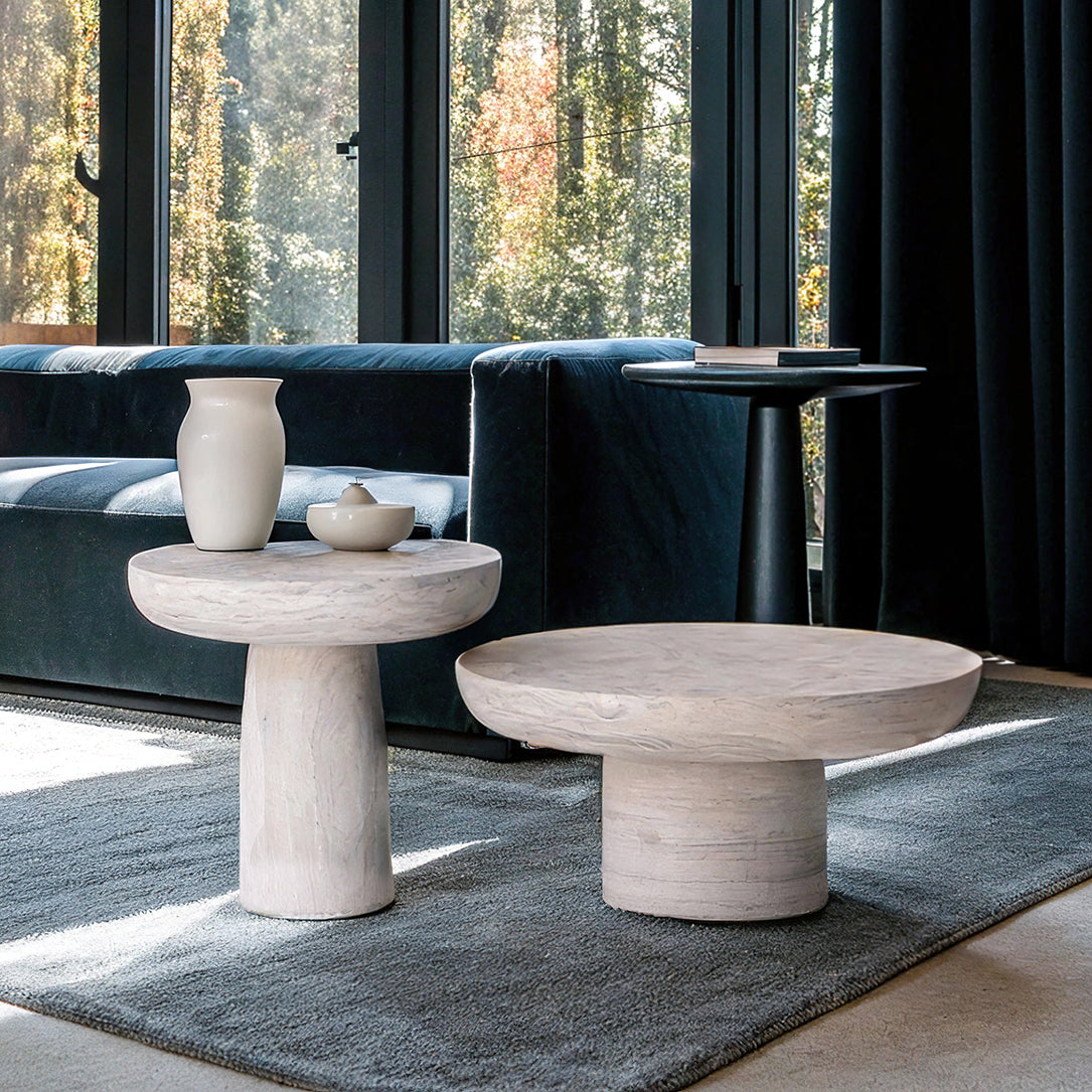 Table basse en travertin massif, au design brut et sophistiqué, mise en scène avec des bougies et une sculpture décorative.