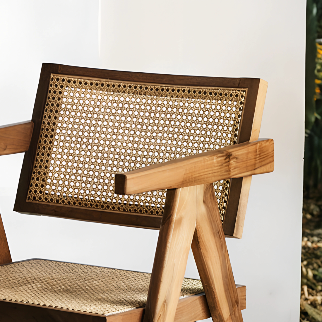 Fauteuil en noyer avec assise et dossier en cannage, au design raffiné et intemporel, accompagné d’un plaid en lin et d’une table d’appoint en pierre.