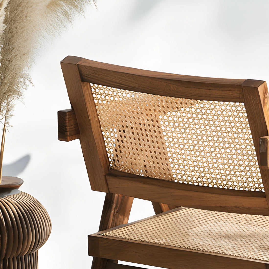 Fauteuil en noyer avec assise et dossier en cannage, au design raffiné et intemporel, accompagné d’un plaid en lin et d’une table d’appoint en pierre.