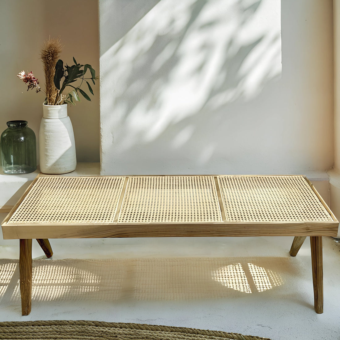 Banc en noyer avec assise en rotin tressé, alliant élégance et authenticité, disposé dans un intérieur chaleureux avec tapis en laine et coussins en lin.
