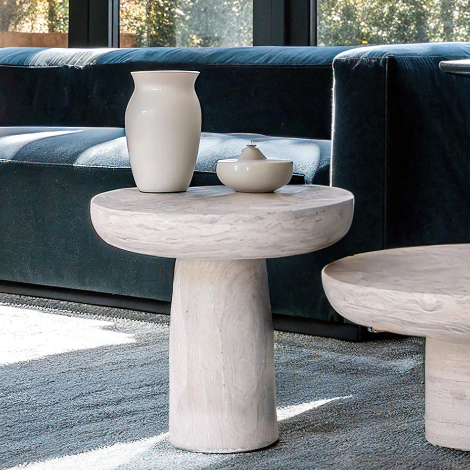 Table basse en travertin massif, au design brut et sophistiqué, mise en scène avec des bougies et une sculpture décorative.