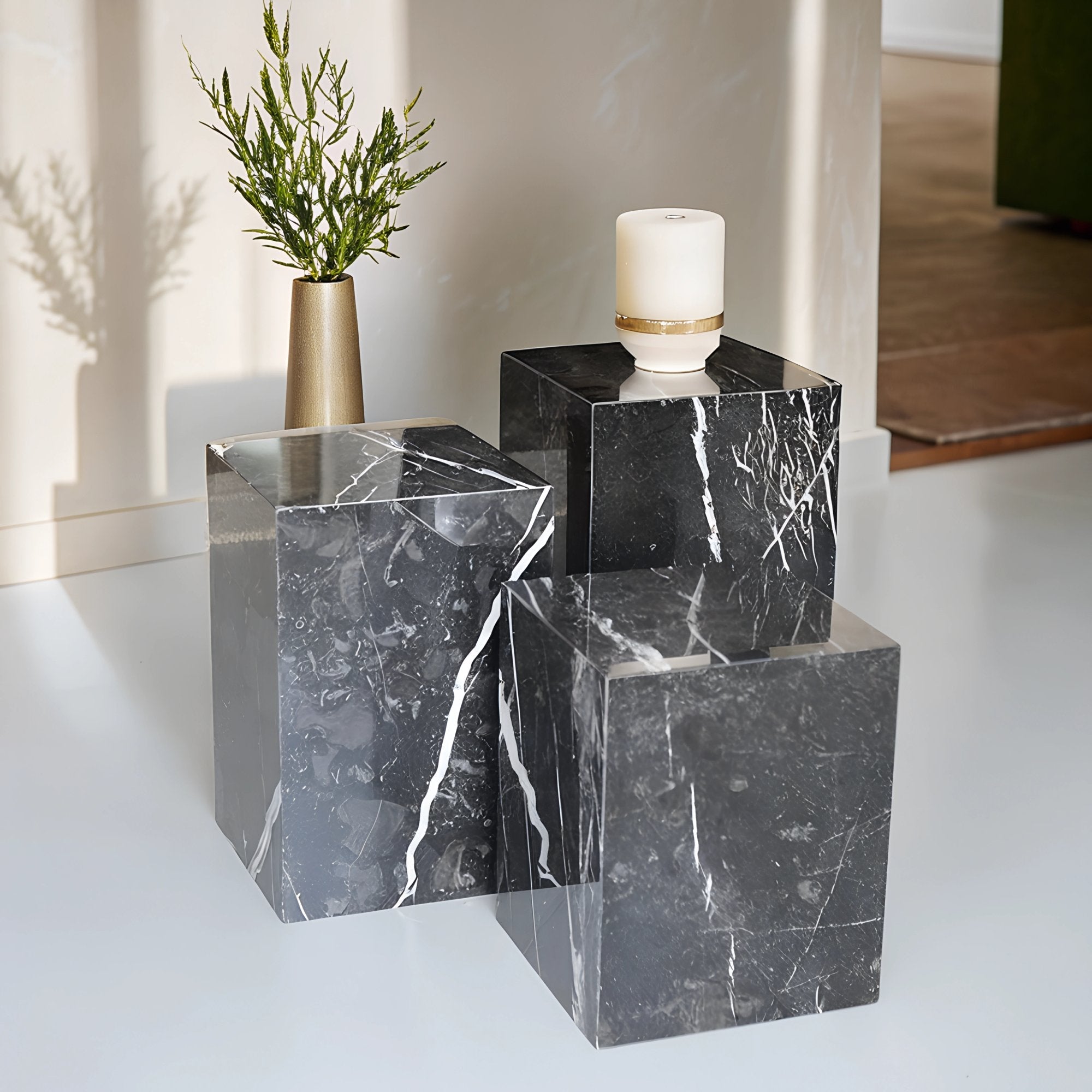 Colonnes en marbre noir avec veinage blanc, utilisées comme tables d’appoint ou piédestaux décoratifs, disposées dans un intérieur moderne avec bougie et plante.