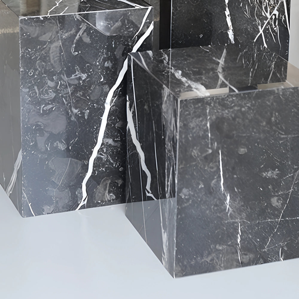 Colonnes en marbre noir avec veinage blanc, utilisées comme tables d’appoint ou piédestaux décoratifs, disposées dans un intérieur moderne avec bougie et plante.