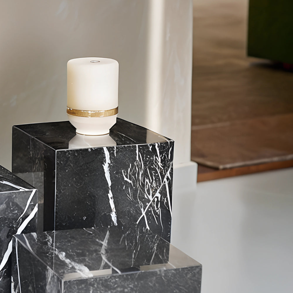 Colonnes en marbre noir avec veinage blanc, utilisées comme tables d’appoint ou piédestaux décoratifs, disposées dans un intérieur moderne avec bougie et plante.